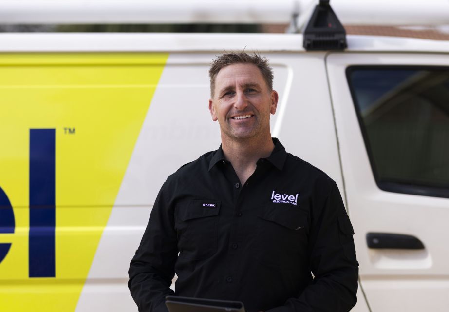 level electrical + air hvac technician smiling and standing in front of work van