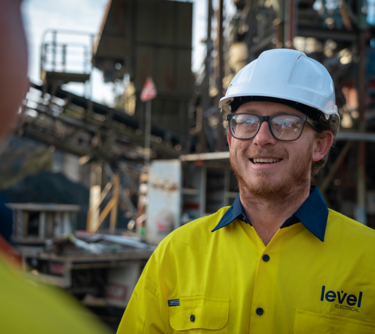 Level Electrical technician wearing safety gear speaking with a colleague on an industrial job site in Australia