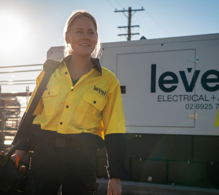 Level Electrical technician walking past generator equipment at a commercial infrastructure site in Australia