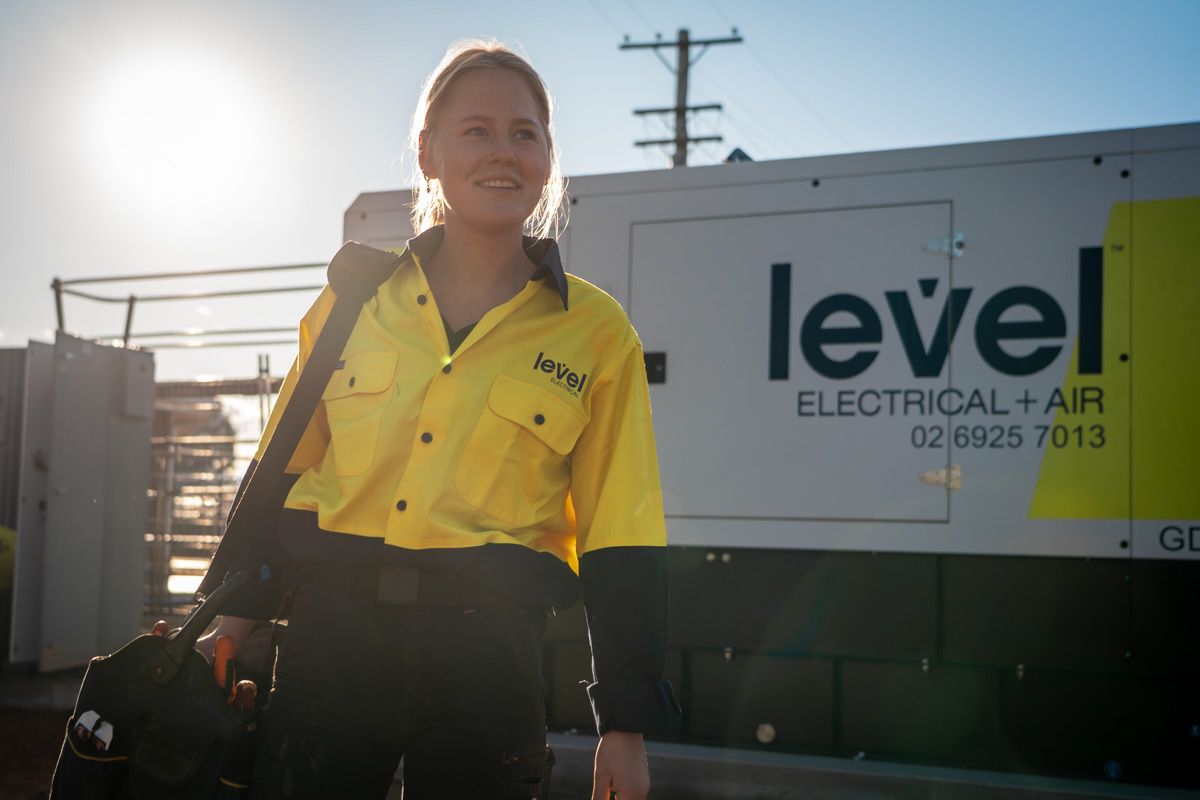 Level Electrical technician walking past generator equipment at a commercial infrastructure site in Australia