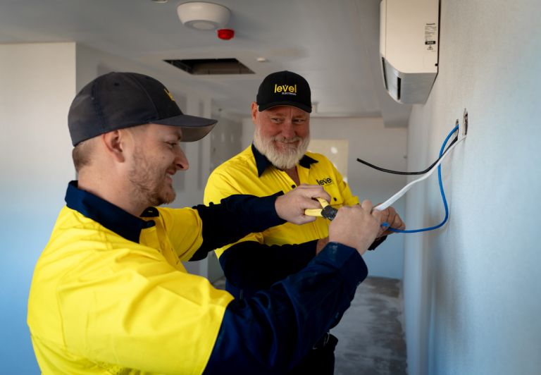 Level electricians connecting wiring for a wall mounted air conditioning unit during installation in Australia