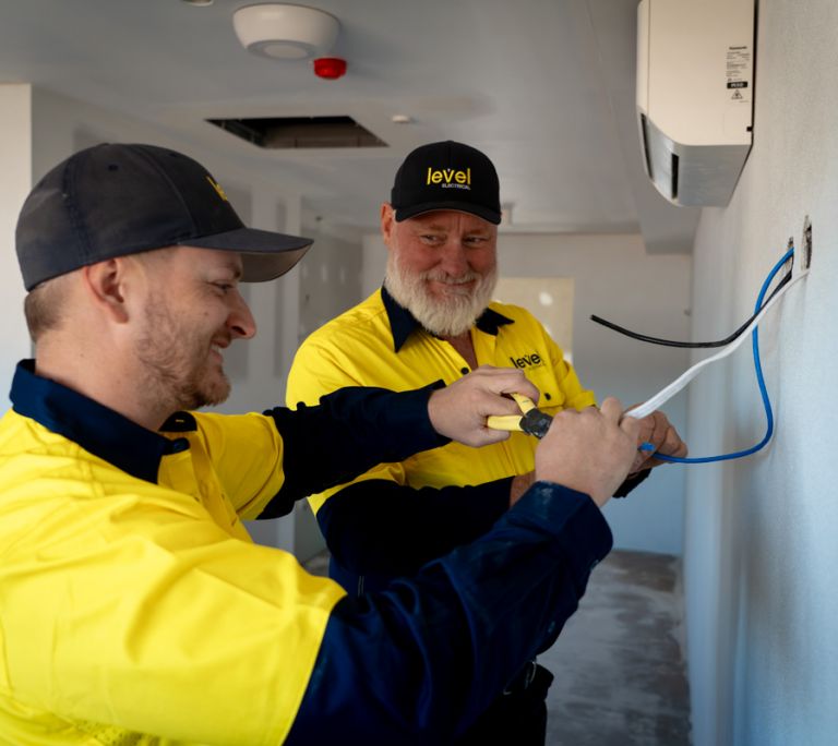 Level electricians connecting wiring for a wall mounted air conditioning unit during installation in Australia