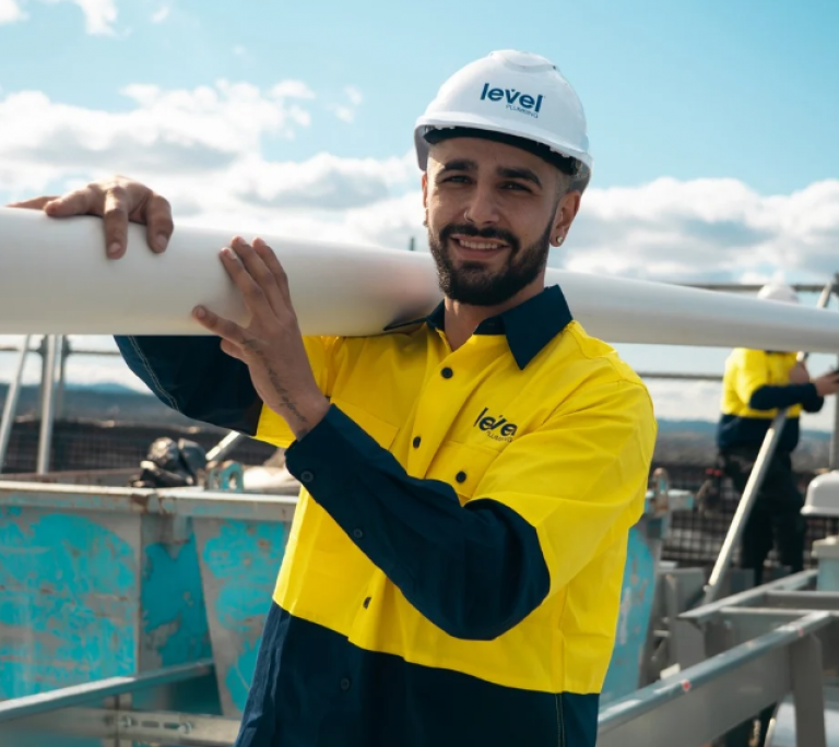 Level plumber carrying pipe while delivering commercial plumbing services in Australia