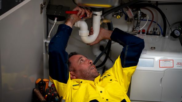 Level plumber inspecting and repairing under sink pipework during a drain issue in Australia