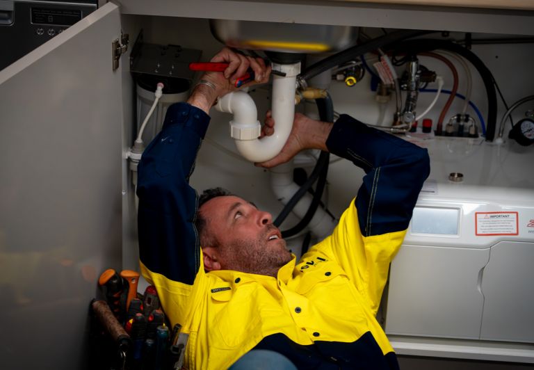 Level plumber inspecting and repairing under sink pipework during a drain issue in Australia