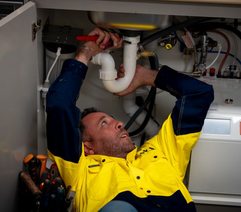 Level plumber inspecting and repairing under sink pipework during a drain issue in Australia