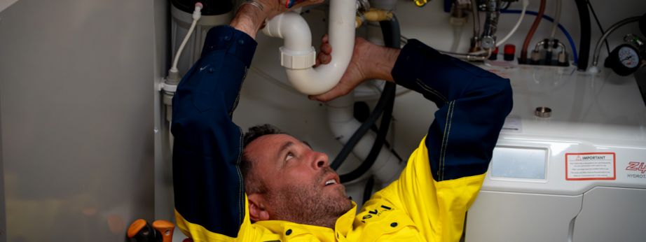 Level plumber repairing pipework under a residential kitchen sink in Australia