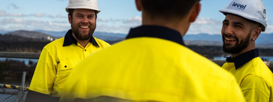 Level plumbing and electrical technicians in safety gear discussing work together on a job site in Australia