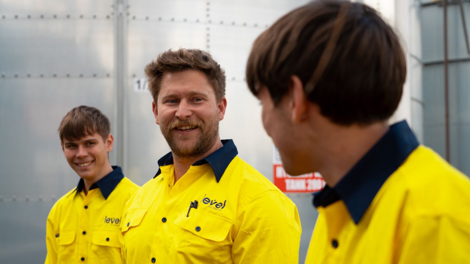 Level plumbing and electrical technicians speaking together on a job site in Australia