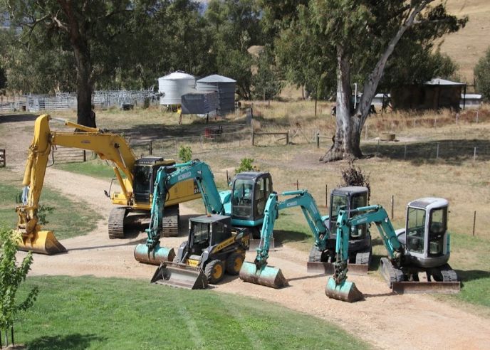 Earthmoving and excavation equipment lined up on a rural driveway, representing civil project capability for Level Plumbing Yea.