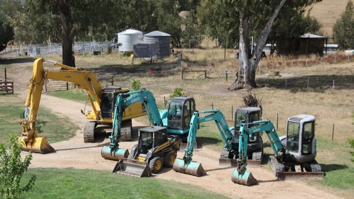 Earthmoving and excavation equipment lined up on a rural driveway, representing civil project capability for Level Plumbing Yea.