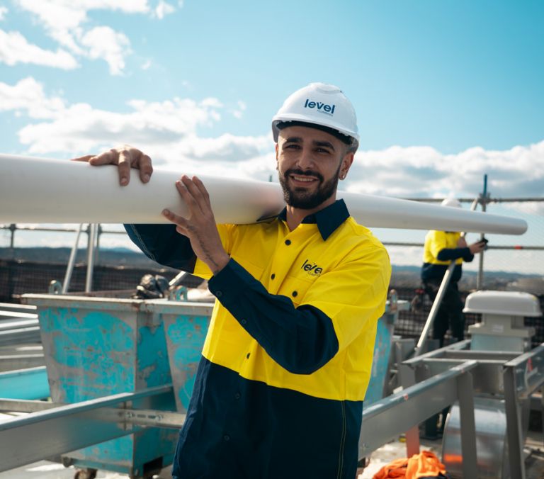 Level Plumbing technician carrying pipework on a construction site in Canberra, representing the skill and professionalism of Level Plumbing Members across Australia.