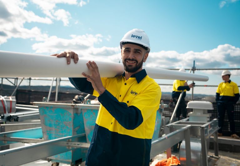 Level Plumbing technician carrying pipework on a construction site in Canberra, representing the skill and professionalism of Level Plumbing Members across Australia.
