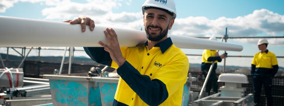 Level Plumbing technician carrying pipework on a construction site in Canberra, representing the skill and professionalism of Level Plumbing Members across Australia.
