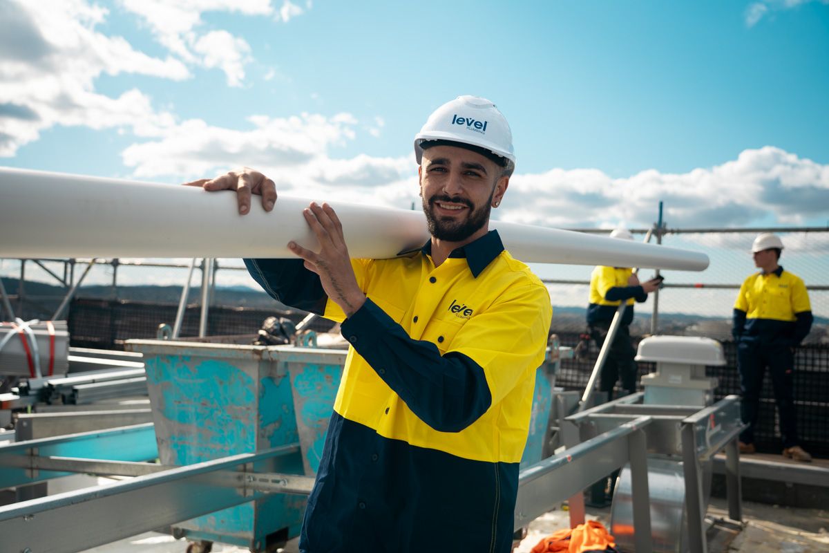 Level Plumbing technician carrying pipework on a construction site in Canberra, representing the skill and professionalism of Level Plumbing Members across Australia.