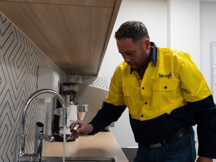 Level Plumbing Canberra technician testing water temperature at a commercial sink to ensure hot water system performance and safety