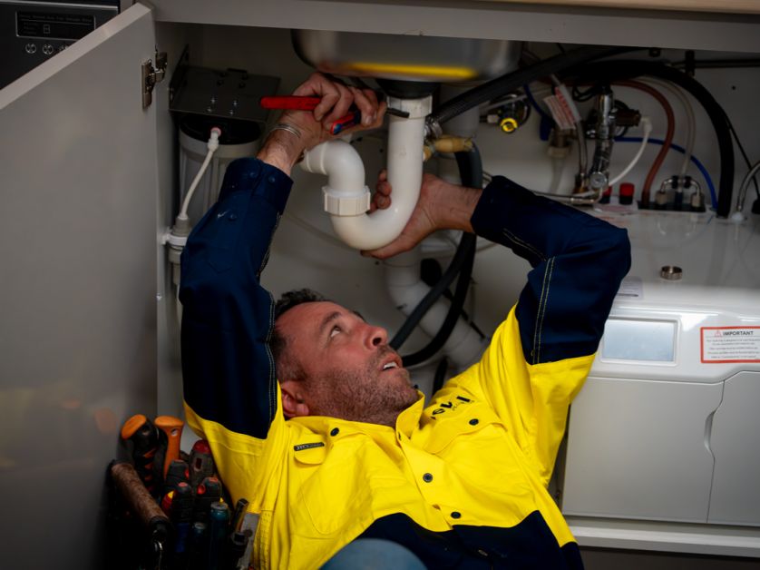 Level Plumbing Canberra technician carrying out residential plumbing maintenance under a kitchen sink, demonstrating reliable local service with national standards.