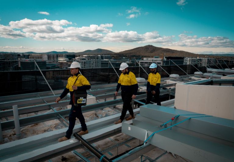 Level Plumbing Canberra technicians walking across a commercial rooftop during roofing and guttering installation in the ACT