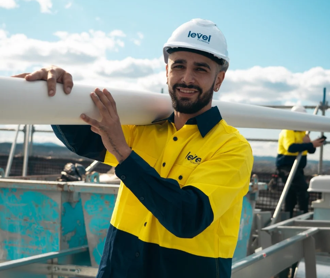 Level Plumbing Canberra technician carrying pipework on a commercial project site in the ACT, representing professional plumbing services across Australia.